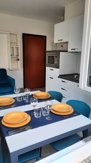 Un espace de vie compact comprenant un coin repas, une kitchenette et une porte donnant sur une autre pièce.