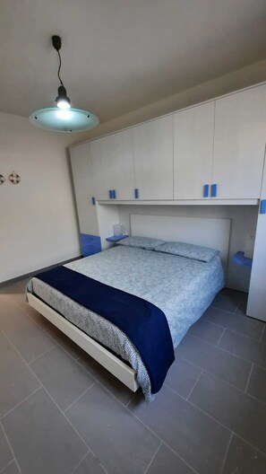 Une chambre à coucher comprenant un lit, des rangements intégrés, un luminaire suspendu et un sol carrelé.