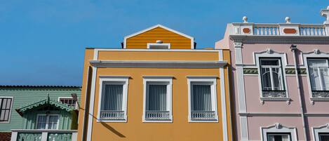 A row of colorful buildings with distinct architectural styles, including a yellow building with white-framed windows and a pink building with decorative moldings.