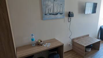 A small room with a wooden desk, two stools, a painting of sailboats, a phone, and a TV mounted on the wall.