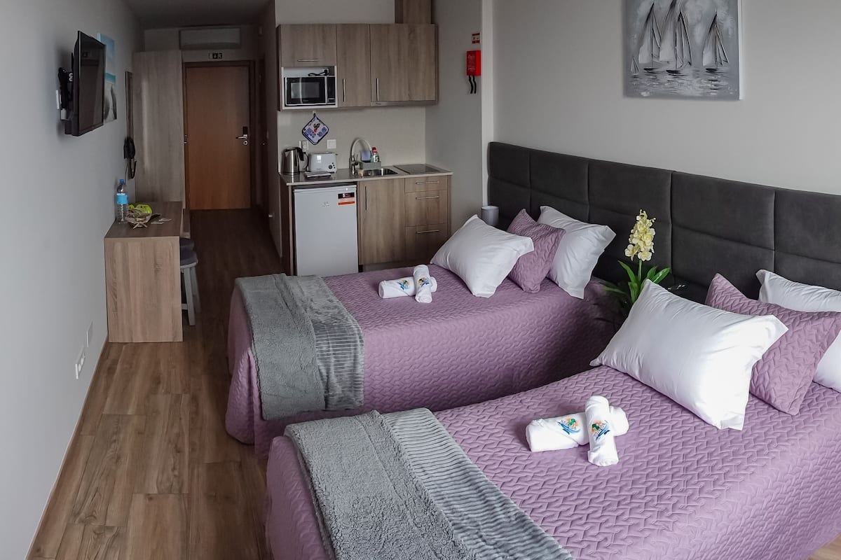 Habitación de hotel con dos camas, kitchenette, baño pequeño y vista al mar.