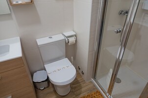 Un baño moderno con inodoro, un cubo de basura pequeño, cabina de ducha de vidrio y suelo de madera.