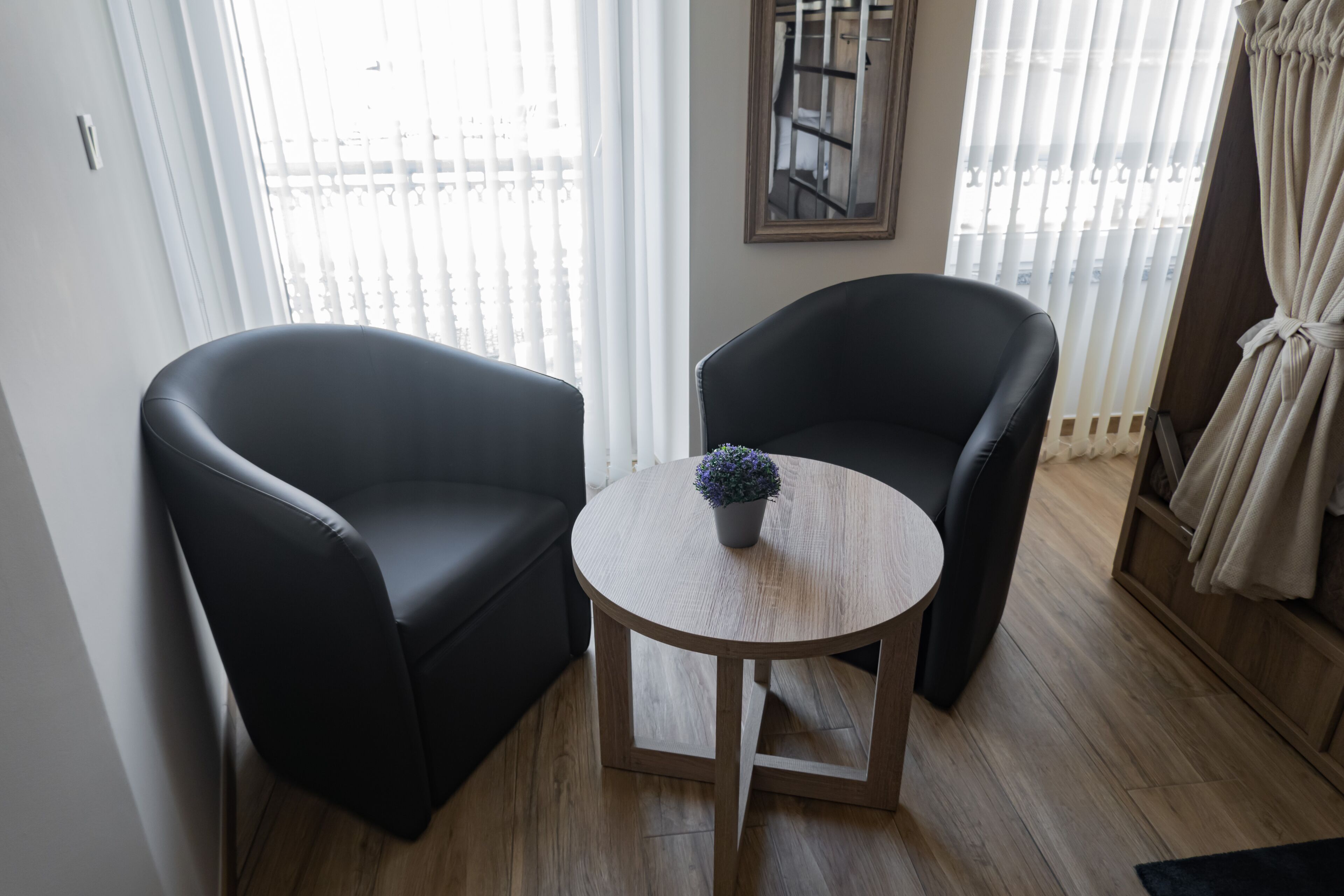 Una habitación con dos sillones negros, una mesita de madera con una planta en maceta y una ventana con persianas.