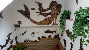 Una escalera con detalles de madera, rodeada de decoraciones marinas fijadas en las paredes, incluyendo una sirena, peces y plantas marinas.