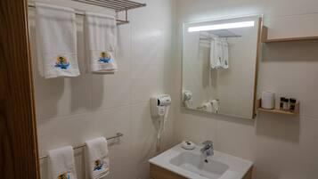 A bathroom with white tiles, a sink, a mirror, and towels with a boat design.