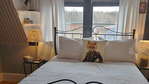 Une chambre à coucher avec un lit, une fenêtre avec des rideaux, une lampe et une étagère décorée d’un motif de poisson.