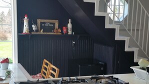 Une cuisine équipée d’une cuisinière à gaz, d’un évier et d’un coin repas avec une chaise. Un escalier mène à un autre niveau.