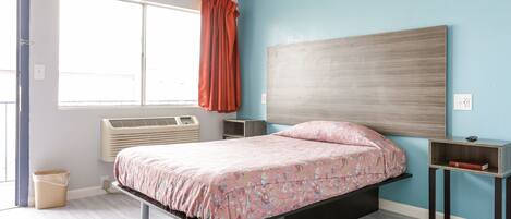 A bedroom with a bed, a window with curtains, a bedside table, and a wall-mounted heater.