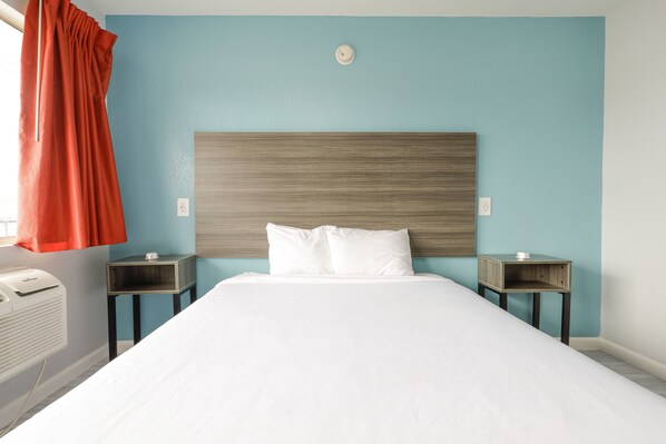 Habitación de hotel con una cama grande, dos mesitas de noche, un calentador en la pared y una ventana con cortina roja.