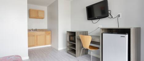 A compact living space with a kitchenette, a flat-screen TV mounted on the wall, a small refrigerator, and a wooden chair.