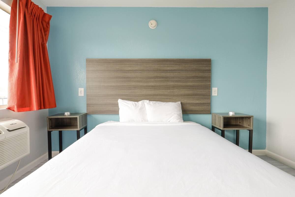 Quarto de hotel com cama, duas mesas de cabeceira, aquecedor fixado na parede e janela com cortinas.