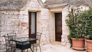 A stone building with a tiled roof, a table with chairs, and potted plants.