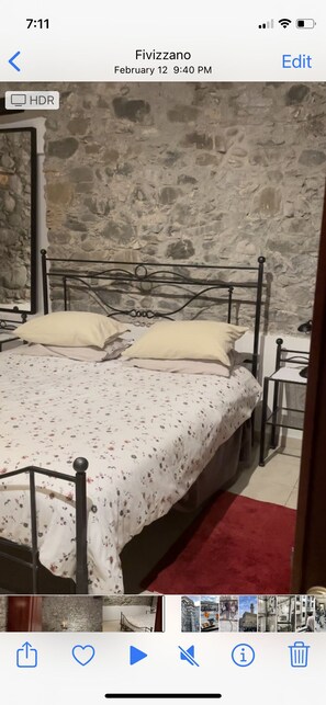 A bedroom with a stone wall, a bed with a floral bedspread, and a red rug. - Romantic Tuscan Riverside Villa (Fivizzano MS)