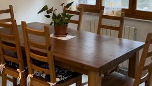 Ein Holztisch mit sechs Stühlen, einer Topfpflanze und einem Fenster mit Vorhängen.