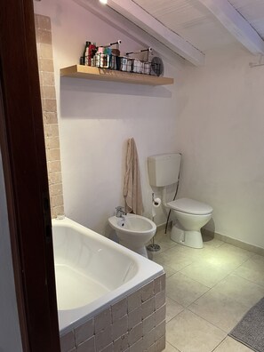 A bathroom with a bathtub, a bidet, and a toilet. There is a shelf above the toilet with various items. - Romantic Tuscan Riverside Villa (Fivizzano MS)