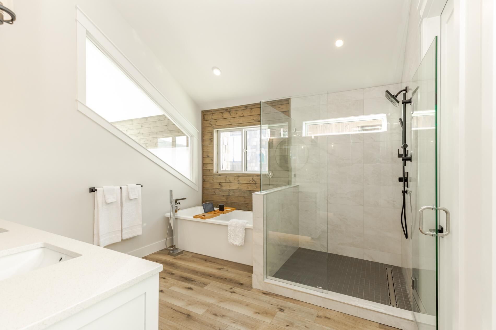 Een moderne badkamer met een douchecabine van glas, een houten wastafelmeubel en een groot raam.