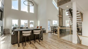 A spacious kitchen with a central island, large windows, and a wooden staircase.