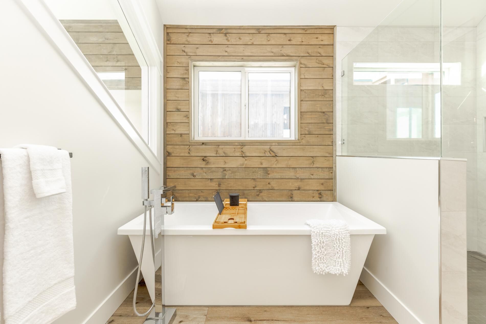 Un baño con pared de paneles de madera, una ventana, una bañera blanca y una cabina de ducha de vidrio.