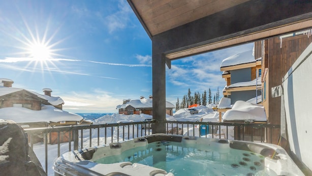 A hot tub on a balcony with a snowy landscape and buildings in the background.