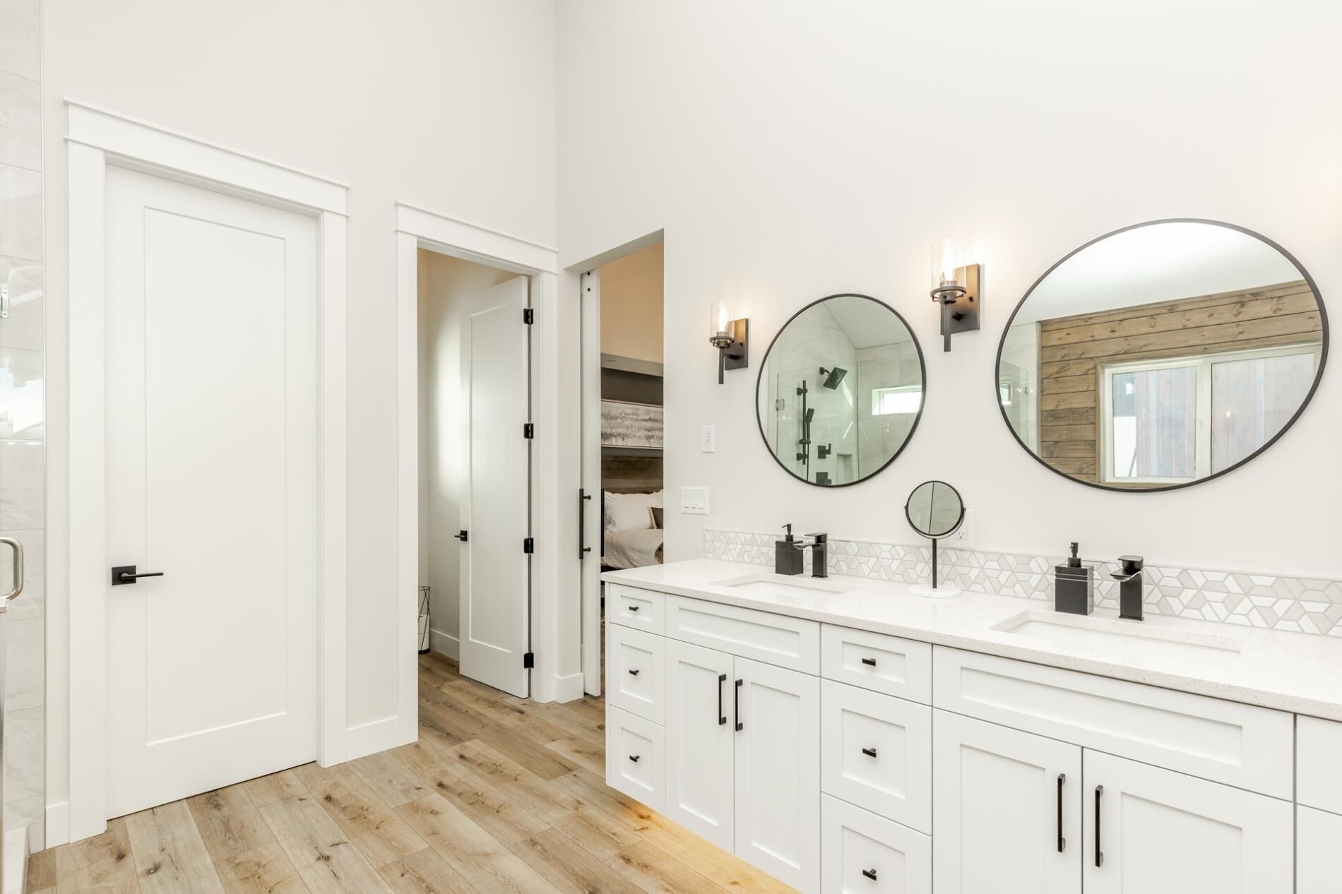 A modern bathroom with white cabinetry, a large mirror, and a wooden floor.