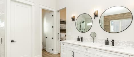 A modern bathroom with white cabinetry, a large mirror, and a wooden floor.