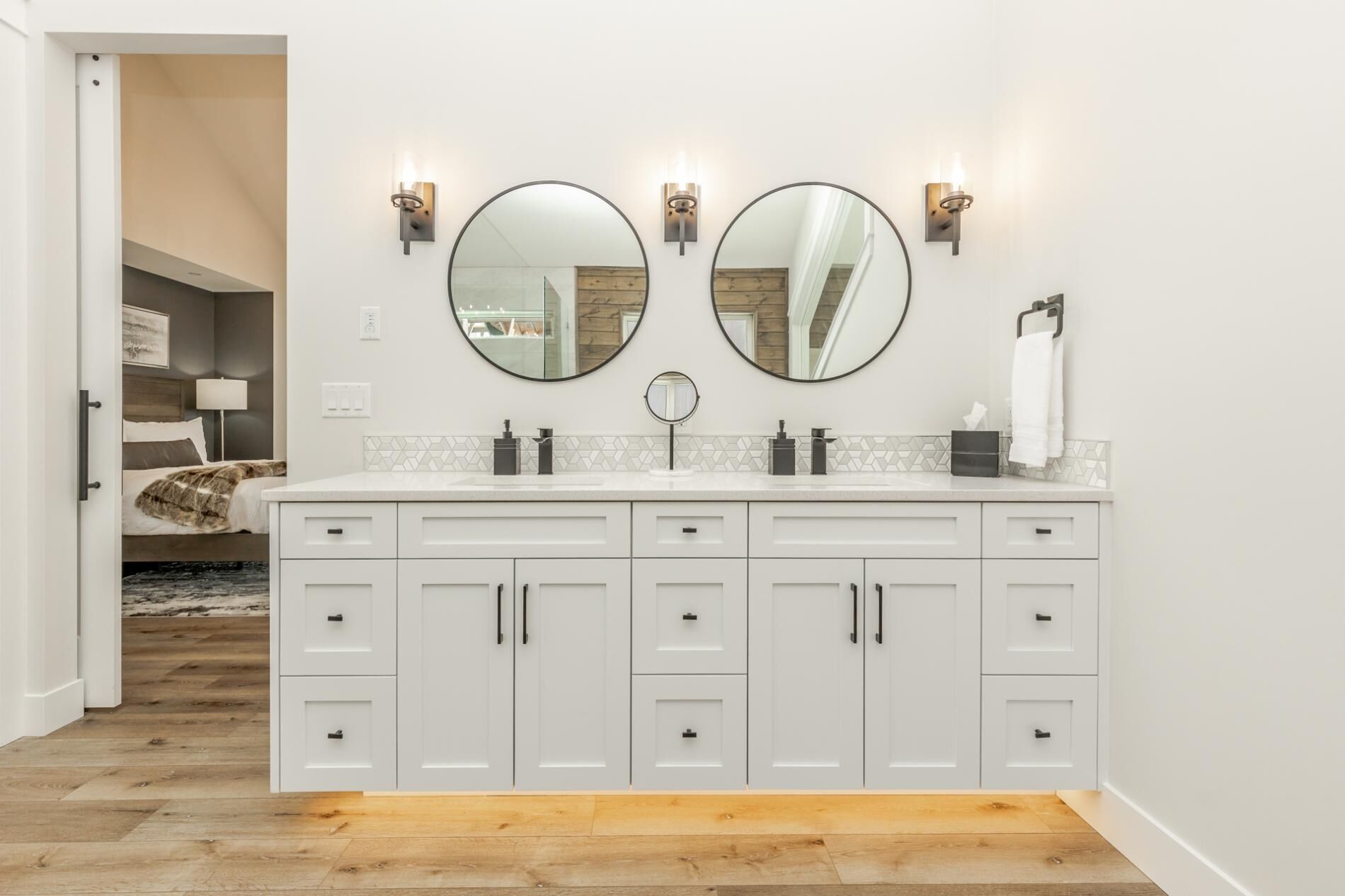 Une salle de bain moderne avec un meuble-lavabo double, deux miroirs fixés au mur et un petit miroir rond placé au-dessus du lavabo.