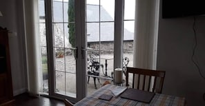 A room with a table set for dining, a chair, and a view of the outside through a glass door.