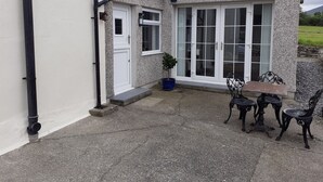 Een gebouw met een witte gevel, een grote glazen deur en een klein terras met een tafel en stoelen.