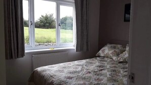 Een slaapkamer met een bed, een raam met gordijnen en uitzicht op een groen veld.