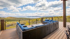 A covered outdoor seating area with wicker furniture and cushions, overlooking a scenic landscape with hills and a clear sky.