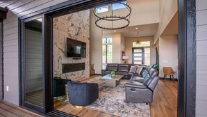 A spacious living room with a large sectional sofa, a flat-screen TV mounted on the wall, and a chandelier.