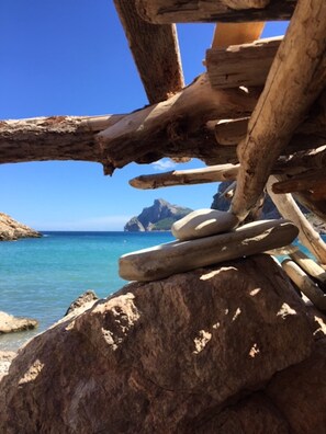 A wooden structure with logs and stones, overlooking a clear blue sea and rocky coastline.