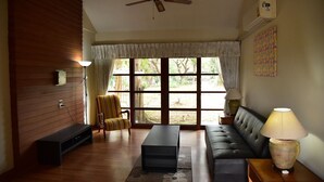 Un salon comprenant un canapé, un fauteuil à rayures, une table basse, un ventilateur de plafond et une grande fenêtre avec des rideaux.