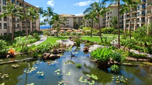 Un hotel con un jardín exuberante, un estanque con nenúfares, palmeras y vistas al océano.