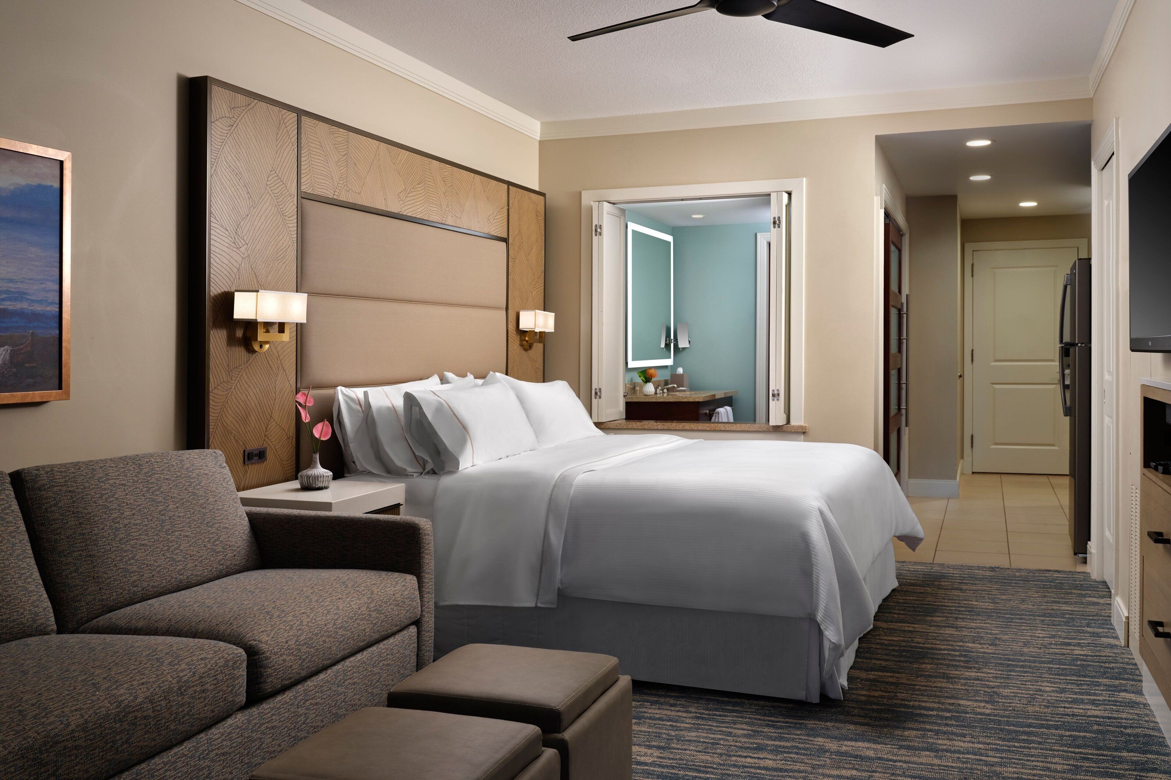 Ein Hotelzimmer mit Bett, einer Couch, einem Fernseher und einem Deckenventilator.