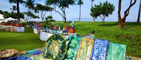 A display of colorful glass art pieces on a grassy area with palm trees in the background.