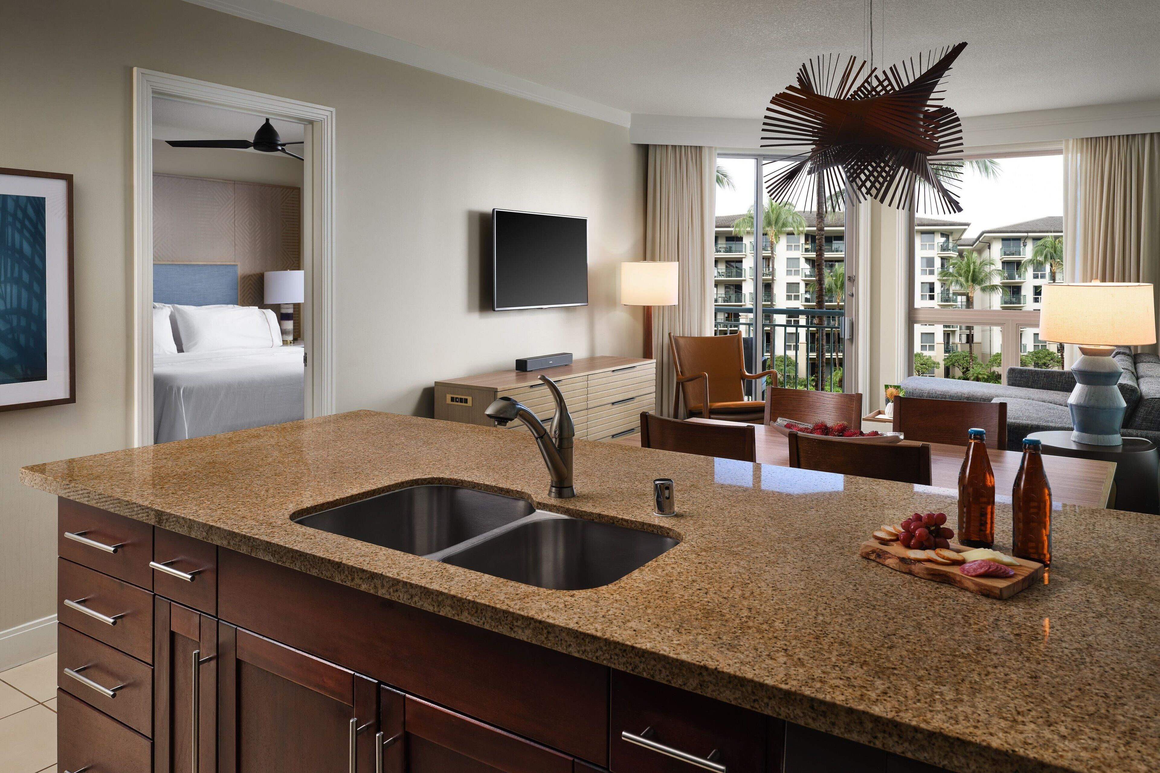 A hotel room with a granite countertop, double sink, and a flat-screen TV mounted on the wall.