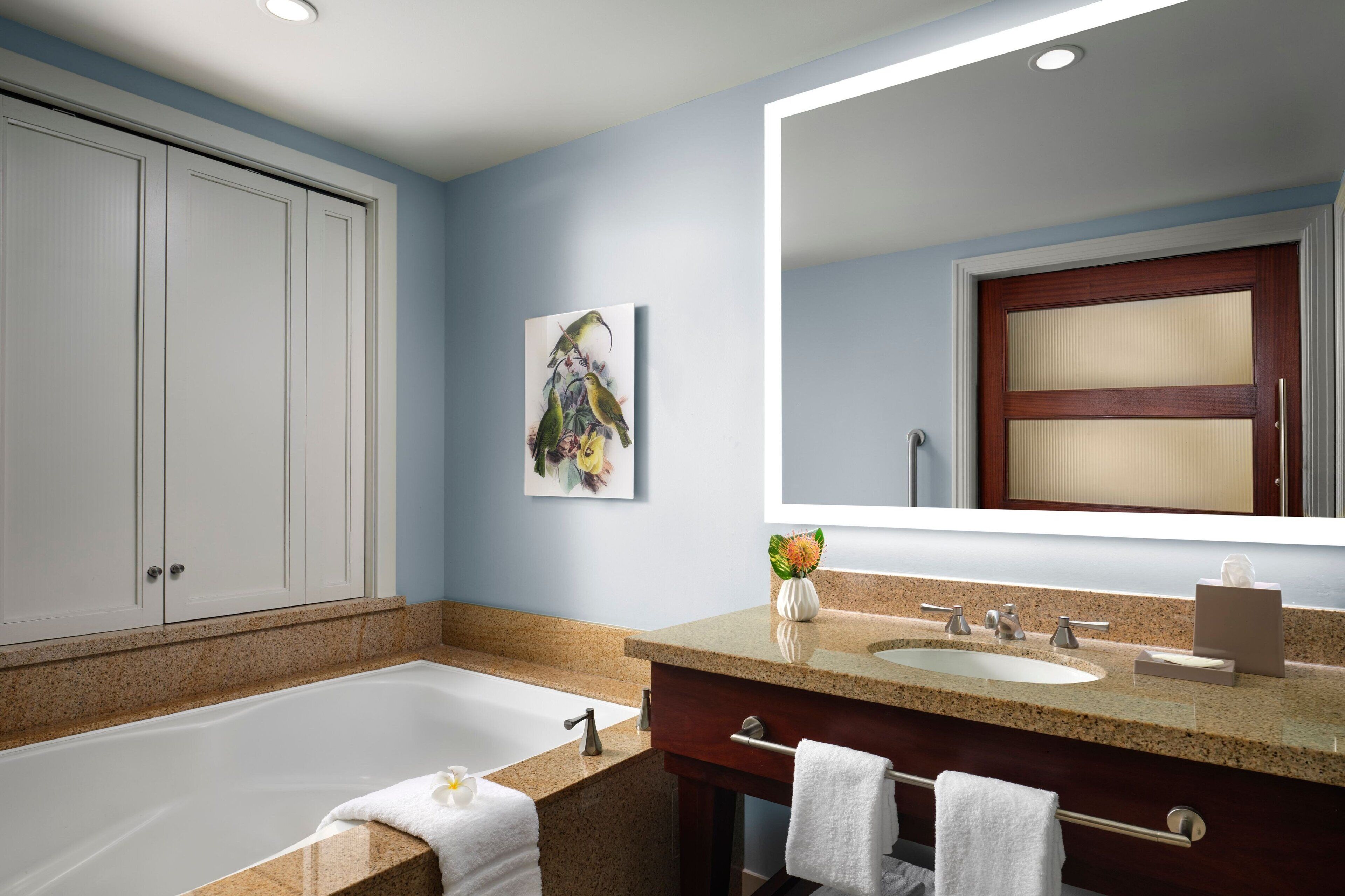 A modern bathroom with a bathtub, two sinks, a large mirror, and a decorative painting on the wall.