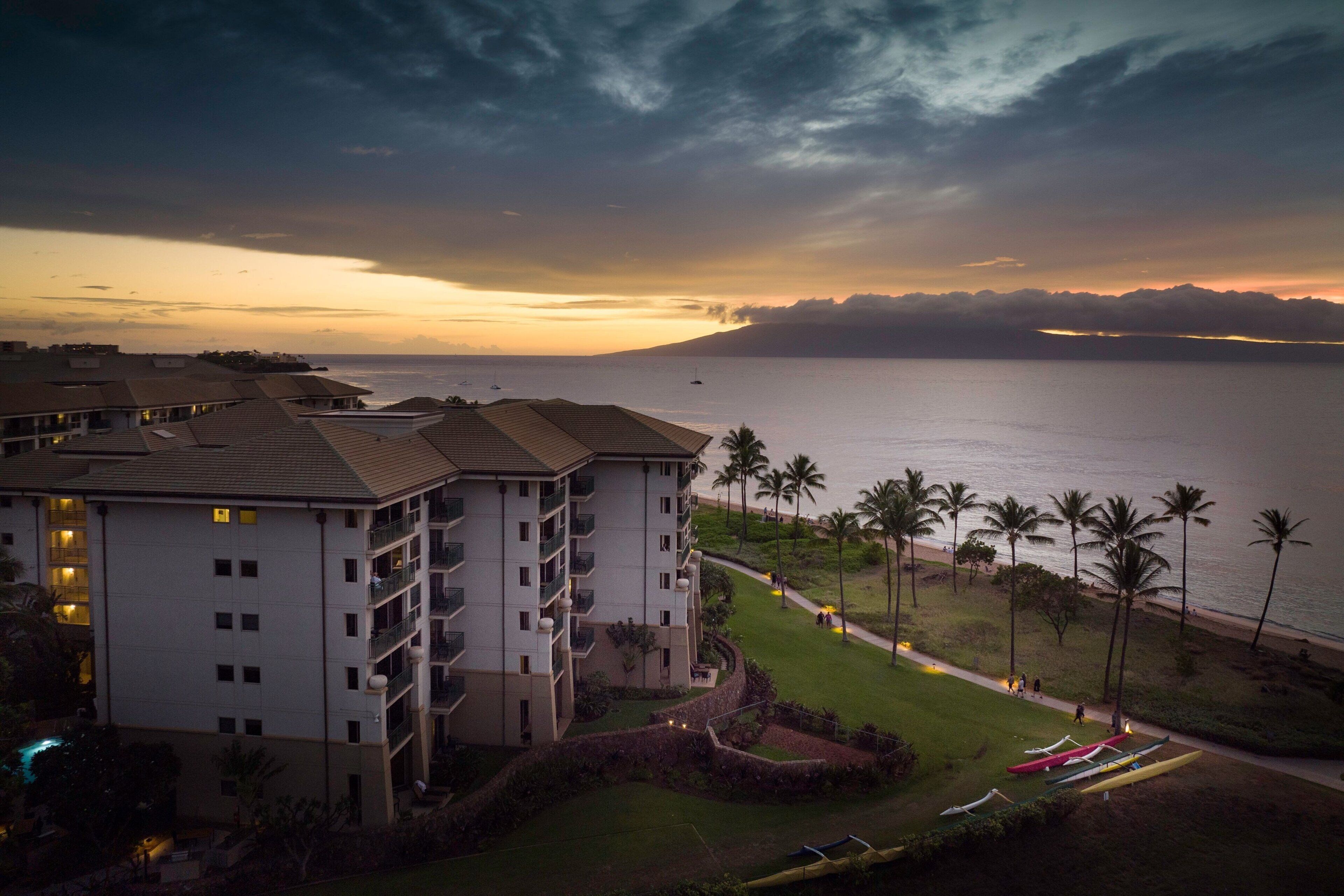 A hotel with multiple floors, a pool, and a view of the ocean at sunset.