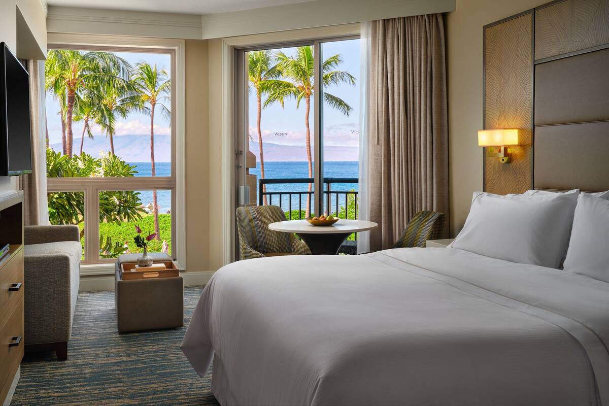 Une chambre d’hôtel avec un grand lit, une petite table sur laquelle se trouve un saladier rempli de fruits, une chaise et un téléviseur.