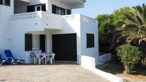 A two-story building with a white exterior, a balcony, and a covered outdoor seating area with chairs and a table.