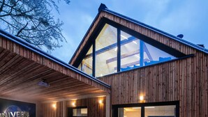 A modern wooden cabin with a large glass window, a bed, and a wall-mounted projector screen.