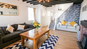 A modern living room with a wooden coffee table, two sofas, a patterned rug, and a staircase with a patterned wall. - Malltraeth Cottage (Bodorgan)