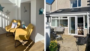 A modern interior with yellow chairs and a star decoration, and a patio with outdoor furniture and a house with a large window. - Malltraeth Cottage (Bodorgan)