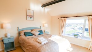 A bedroom with a bed, nightstands, a window with curtains, and a view of the outside. - Malltraeth Cottage (Bodorgan)