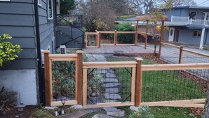 Un patio trasero con valla de madera, sendero de piedra y una casa de fachada gris.