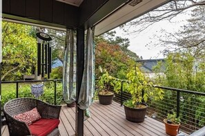 Une terrasse en bois agrémentée de plantes en pot, une chaise en osier avec un coussin rouge et une rambarde en métal.