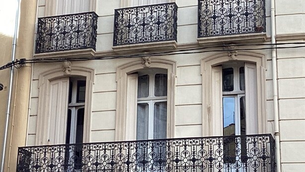 Un edificio con tres ventanas y balcones ornamentales de hierro forjado negro.