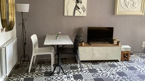Una habitación con una mesa blanca, una silla negra, un armario blanco, un televisor y baldosas de suelo con diseño.