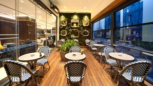 Un espace extérieur moderne, aménagé avec des tables et des chaises rondes, entouré de murs de verre et offrant une vue sur la ville.